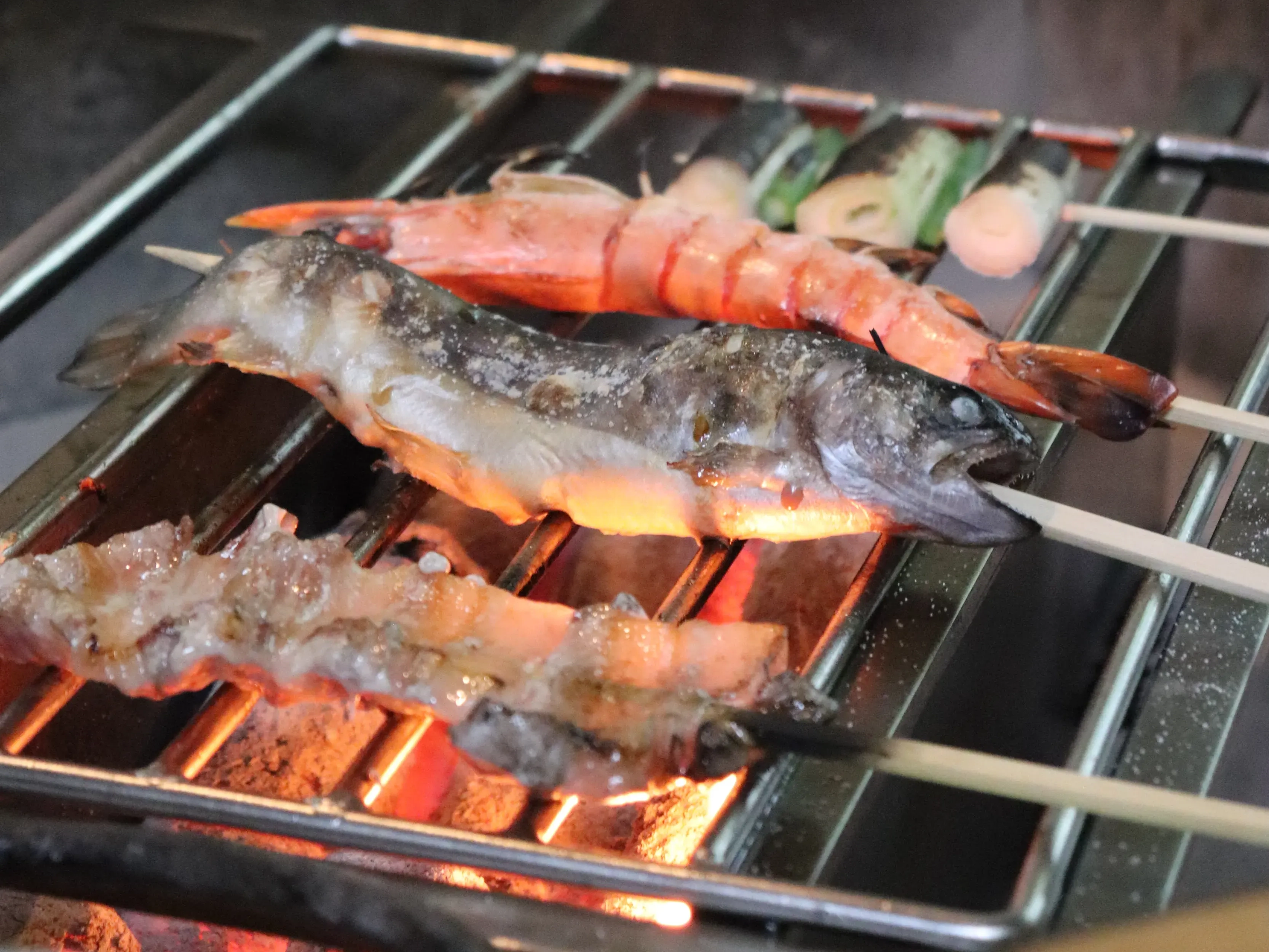 炭火の網の上でジューシーに焼き上がる、貯水池鳥山のこだわりの地鶏と新鮮な川魚